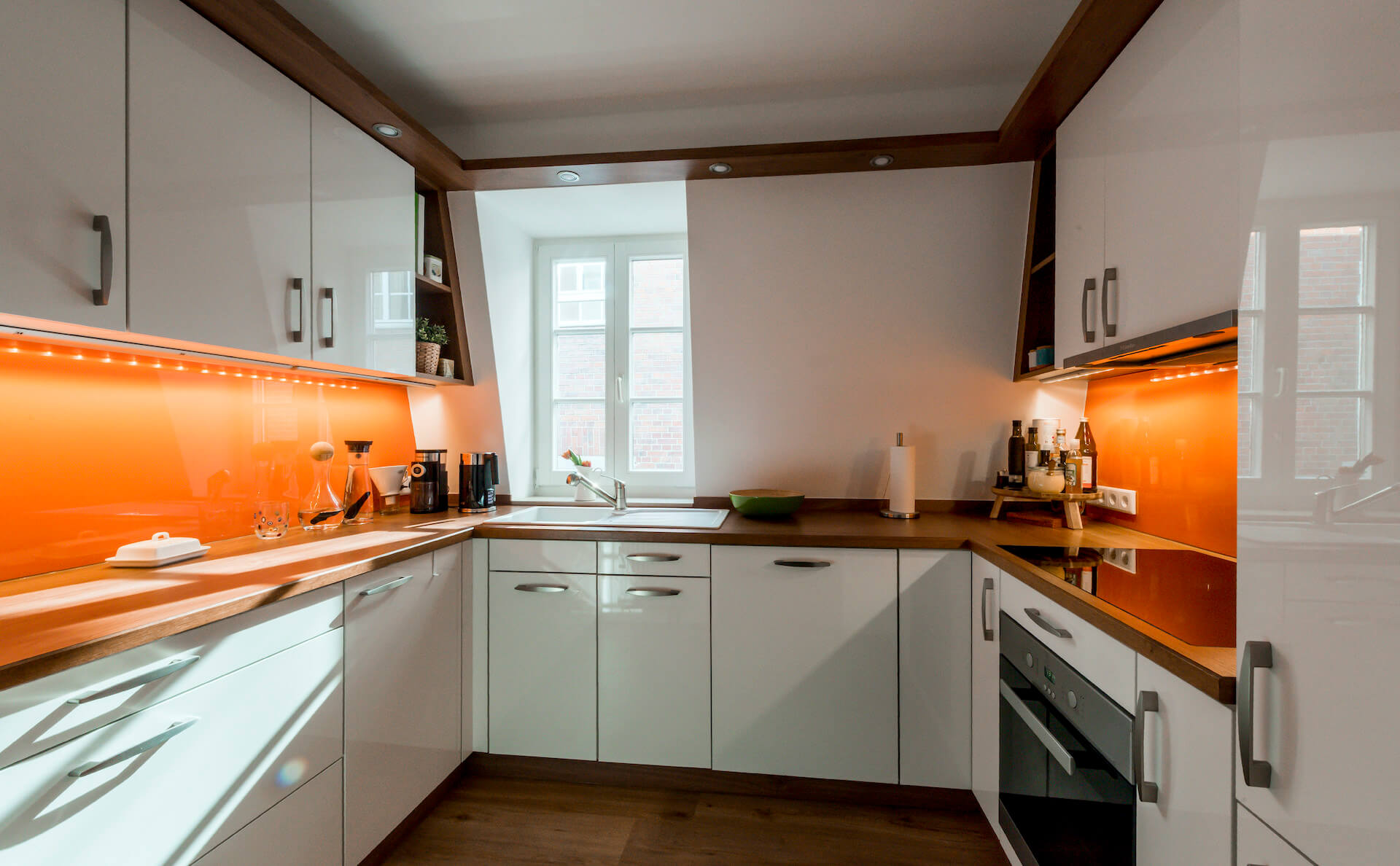 Küche in hochglänzendem Weiß mit orange farbener Rückwand
