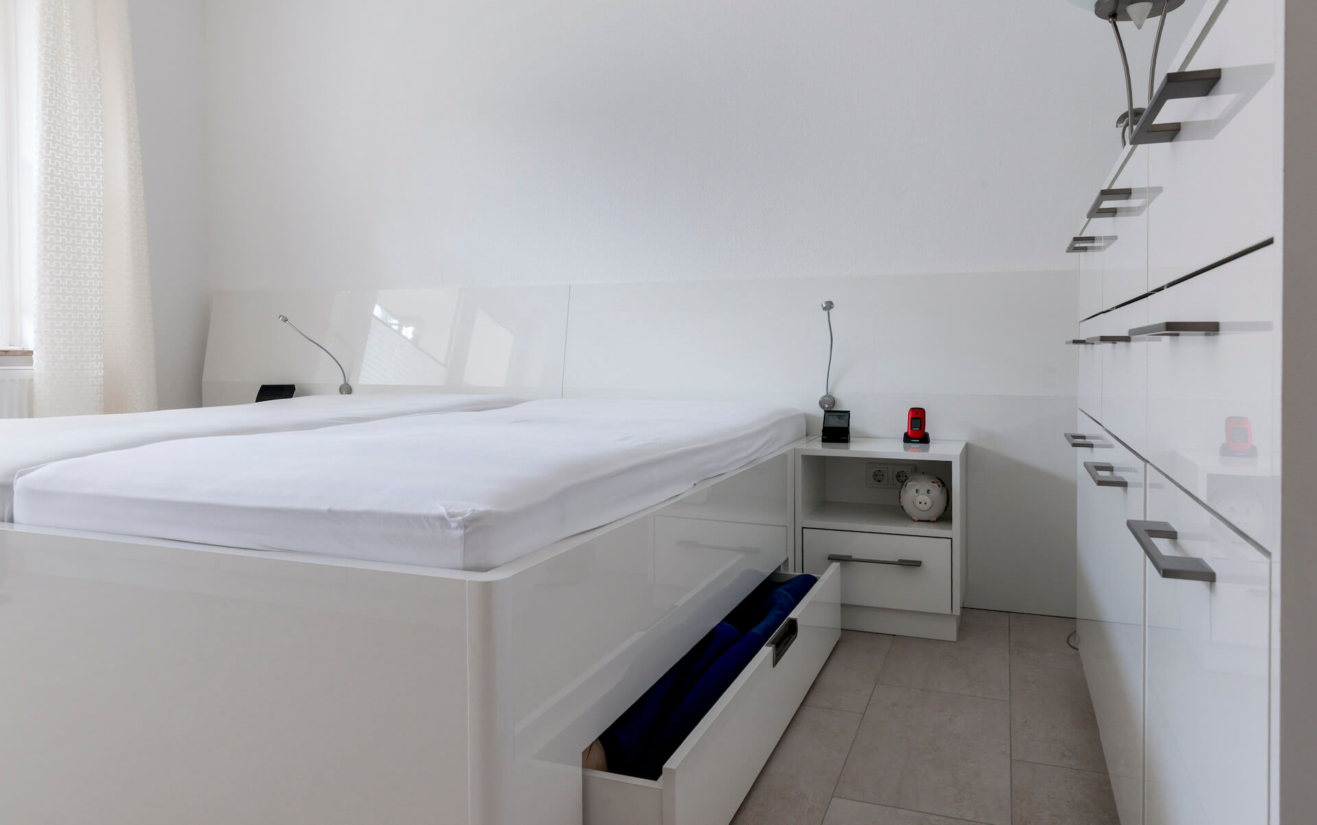 Schlafzimmer in hochglänzendem Weiß mit zusätzlichem Stauraum in den beiden Schubladenelementen unter dem Bett